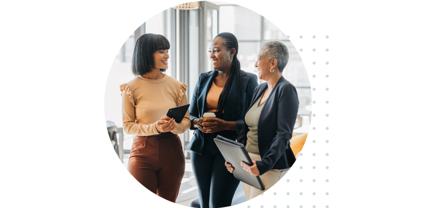 Three women engaged in conversation in a professional environment.